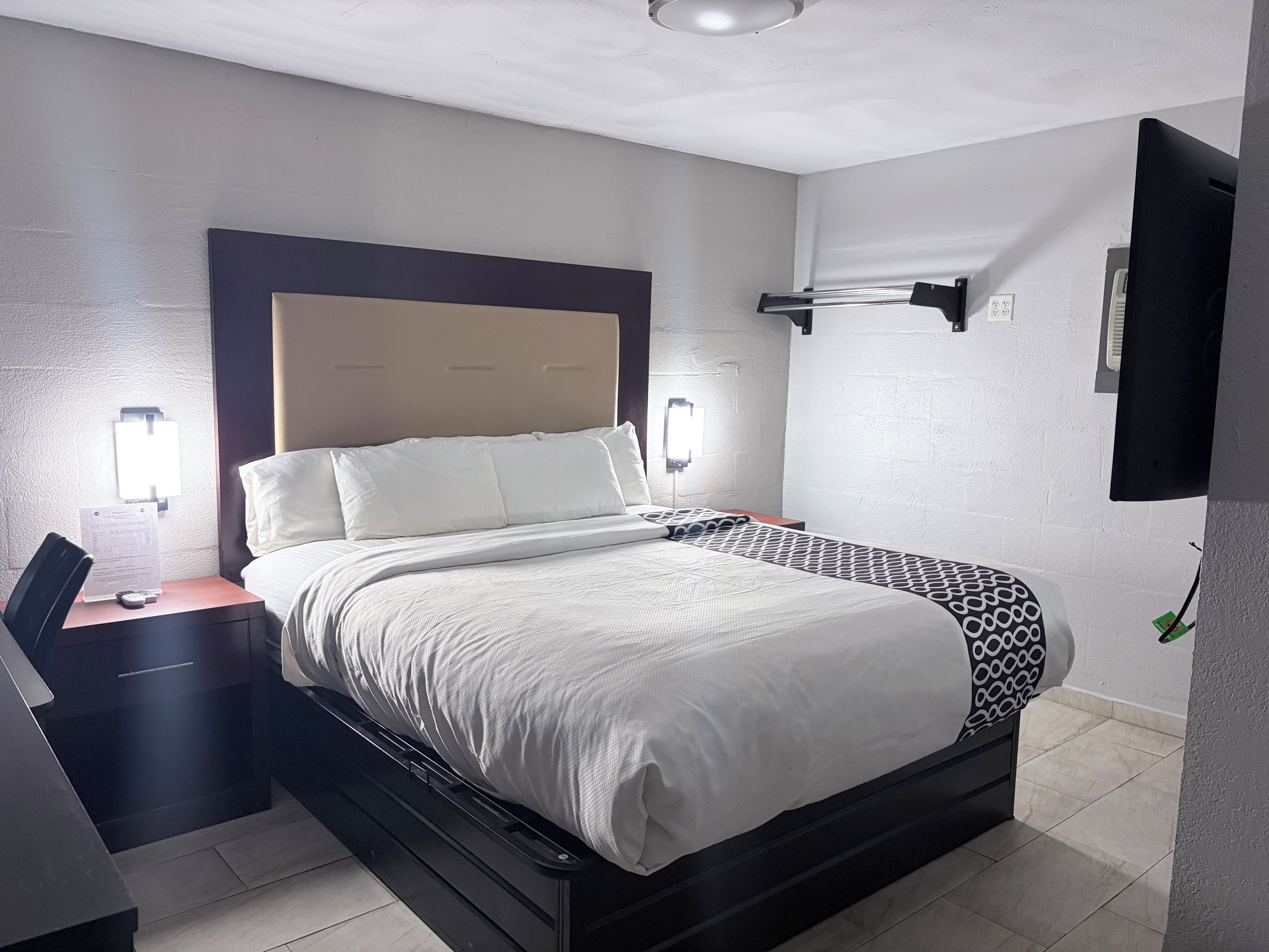 A hotel room with a bed, bedside table, lamp, and a wall-mounted TV.