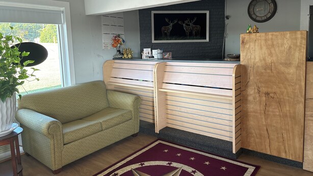A room with a green sofa, a wooden bench, a clock, and a wall-mounted shelf with decorative items. - Budget Inn (Nocona)