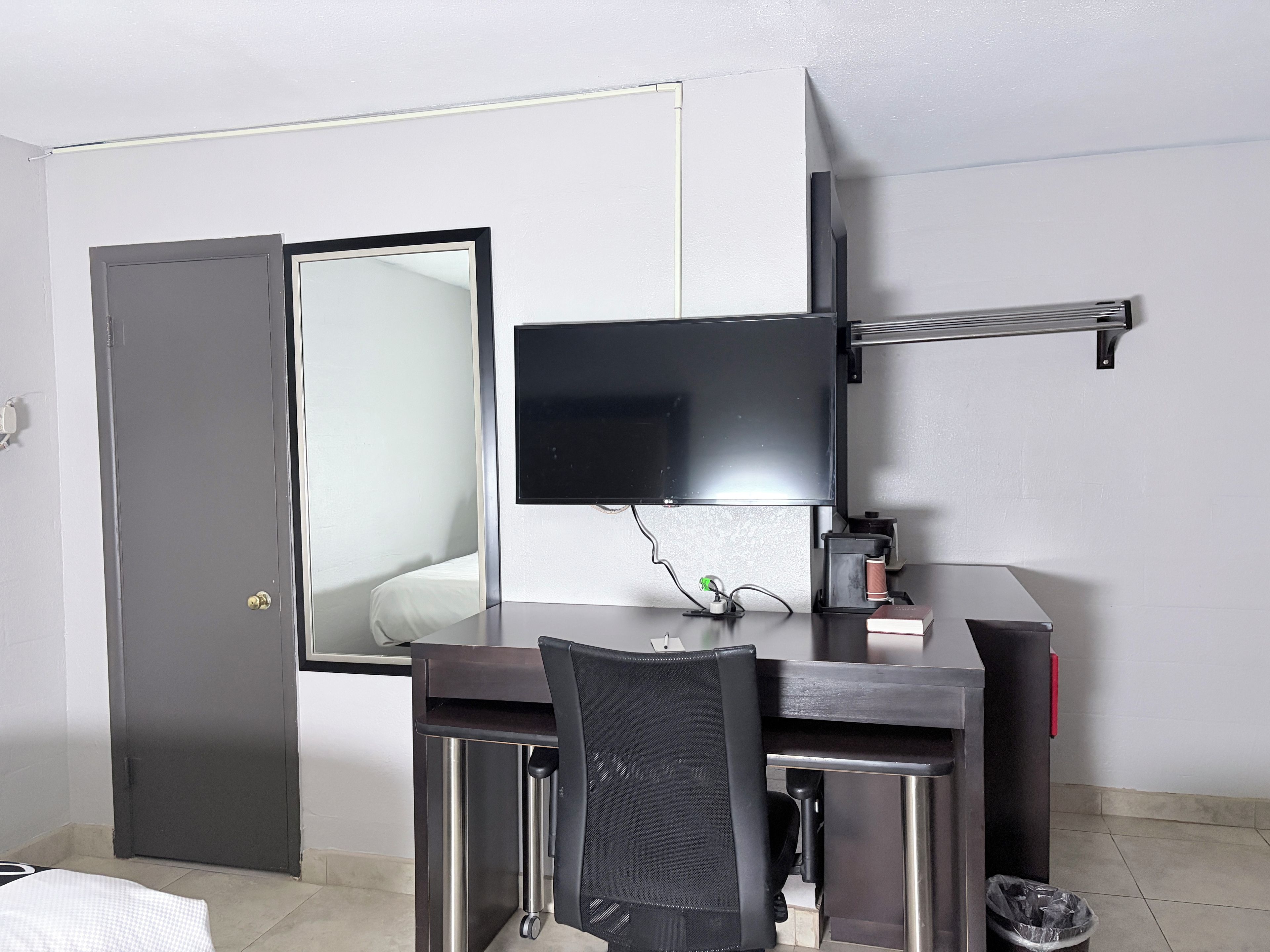 Une chambre d’hôtel compacte, équipée d’un bureau, d’une chaise et d’un téléviseur à écran plat fixé au mur.