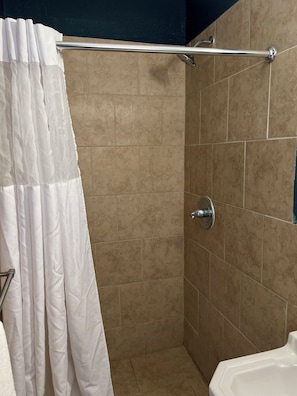 A shower area with beige tiles, a white curtain, and a metal grab bar. - Budget Inn (Nocona)