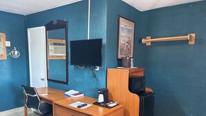 A room with a wooden desk, a black chair, a mirror, a television, and a microwave. - Budget Inn (Nocona)