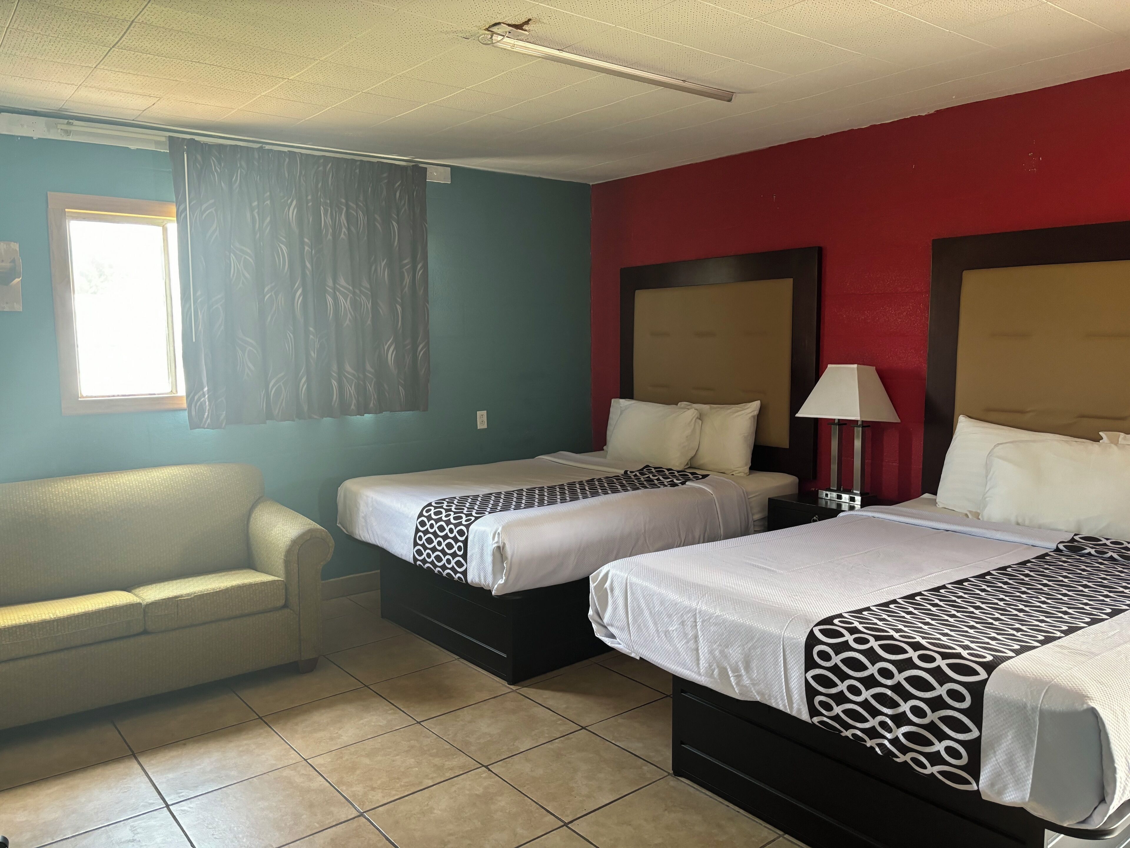 A hotel room with two beds, a sofa, and a window with curtains.