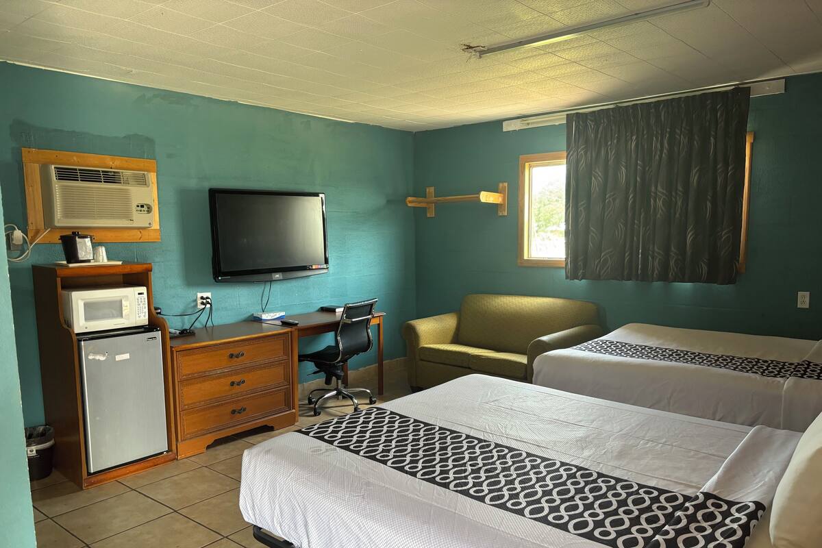 A hotel room with two beds, a desk with a chair, a television, a microwave, and a refrigerator.