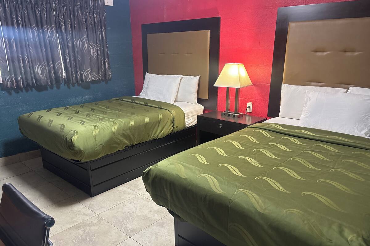 A hotel room with two beds, a nightstand with a lamp, and a chair.