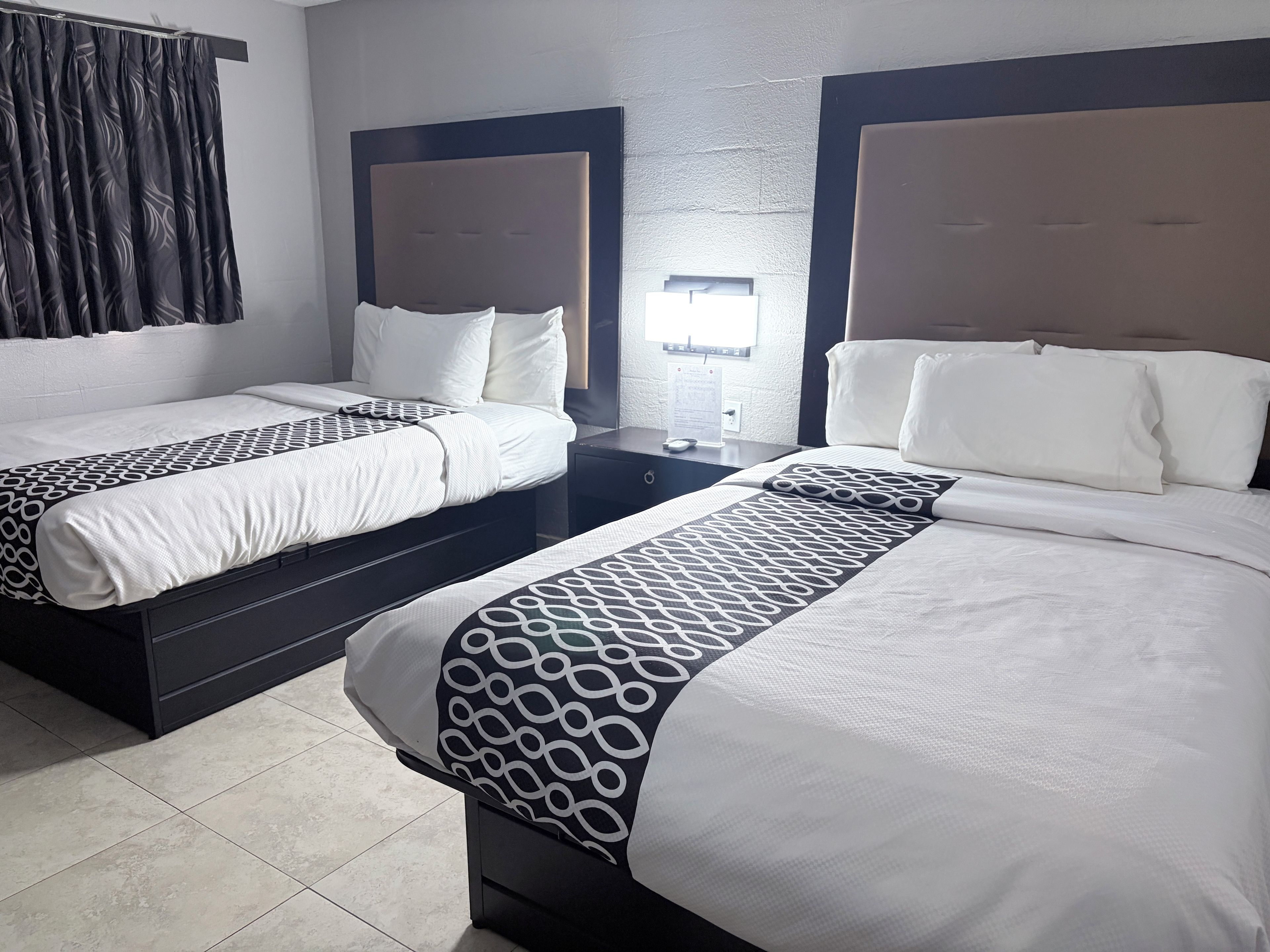 Ein Hotelzimmer mit zwei Betten, jeweils mit Kopfteil, Nachttisch und Vorhang.