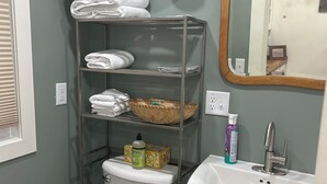 Een badkamer met toilet, een plank met opgevouwen handdoeken, een ventilator, een spiegel en een wastafel.