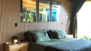 A modern bedroom with a wooden floor, a bed with green bedding, a nightstand with a plant, and a large window with a view of mountains. - Pepper Jack Shack: Your Cozy Mountain Retreat (Newport)