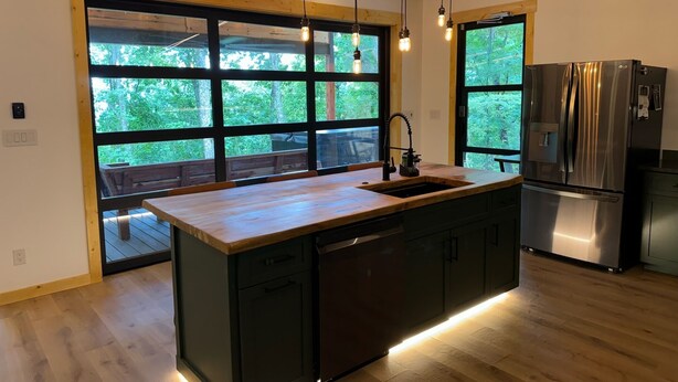 A modern kitchen with a large island, stainless steel appliances, and large windows offering a view of the outdoors. - Pepper Jack Shack: Your Cozy Mountain Retreat (Newport)