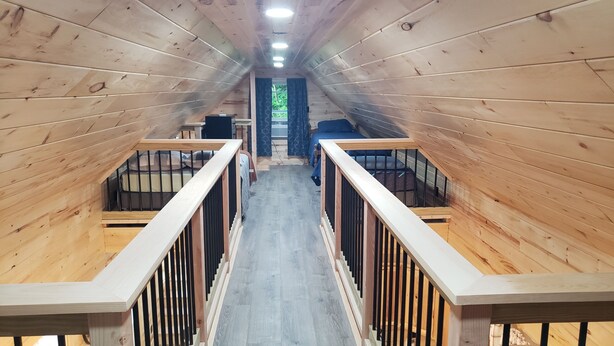 A wooden interior with a central staircase, railings, and a window with curtains. - Bear Cabin: Charming 2-bedroom cabin with WiFi, AC in marvelous Sebec (Sebec)