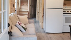 A cozy cabin interior with a sofa, a refrigerator, and wooden walls. - Bear Cabin: Charming 2-bedroom cabin with WiFi, AC in marvelous Sebec (Sebec)