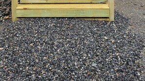 A wooden cabin with a porch, a red Adirondack chair, and a gravel driveway. - Bear Cabin: Charming 2-bedroom cabin with WiFi, AC in marvelous Sebec (Sebec)