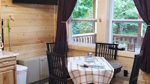 A cozy cabin interior with a wooden interior, a dining table with chairs, a television mounted on the wall, and a window with curtains. - Bear Cabin: Charming 2-bedroom cabin with WiFi, AC in marvelous Sebec (Sebec)