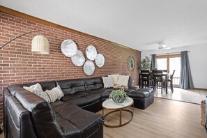 Ein modernes Wohnzimmer mit einer ledernen Eckcouch, einem runden Couchtisch und einem Essbereich mit Tisch und Stühlen.