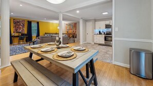 A dining area with a wooden table set for four, a bench, and a modern kitchen in the background. - Durham 4BR/3BA: Game Room, Pool, Art! Sleeps 10 (Durham)