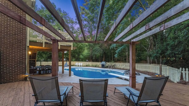 A wooden deck with three chairs, a pool, and a pergola. - Durham 4BR/3BA: Game Room, Pool, Art! Sleeps 10 (Durham)