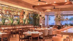 Um restaurante amplo com mobiliário de madeira, um espaço de bar e grandes janelas com vista para o oceano.