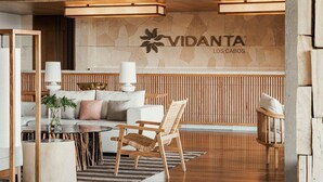 Uma área de recepção moderna com parede de pedra, painéis de madeira e o logotipo da VIDANTA LOS CABOS.