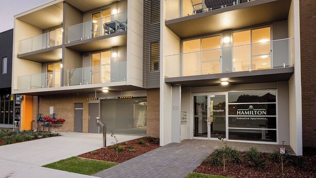 A modern apartment building with multiple balconies, a reception area, and a garage. - One Bedroom Apartment (Hamilton)