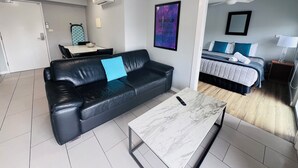 A modern living room with a black leather sofa, a marble coffee table, and a dining area with a table and chairs. - One Bedroom Apartment (Hamilton)