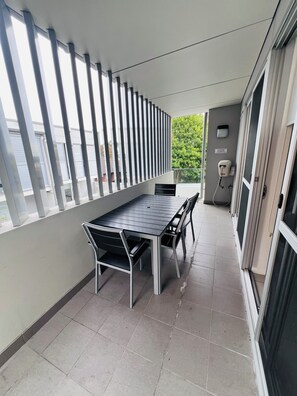 Relax on the balcony with a long table and matching chairs, surrounded by a green outdoor area.