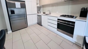 A modern kitchen with white cabinets, a stainless steel refrigerator, a dishwasher, a gas stove, and a built-in oven. - One Bedroom Apartment (Hamilton)
