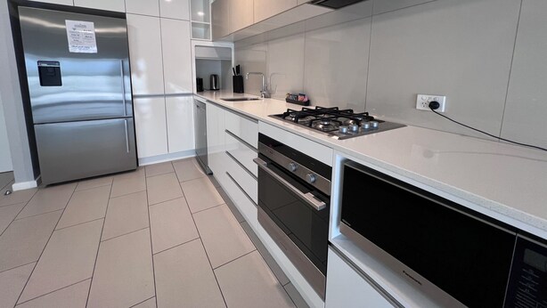 Una cocina moderna con electrodomésticos de acero inoxidable, armarios blancos y salpicadero de azulejos.