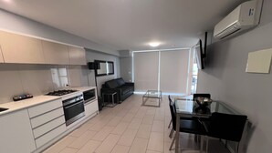 Una cocina moderna con comedor, un sofá negro y un televisor montado en la pared.