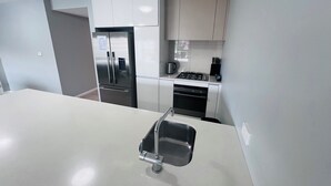 A modern kitchen with stainless steel appliances, a white countertop, and light-colored cabinets. - Two Bedroom Apartment (Hamilton)
