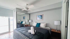 Ein Hotelzimmer mit einem großen Bett, zwei Nachttischen mit Lampen, einem Deckenventilator, einem großen Spiegel und einem Gemälde an der Wand.