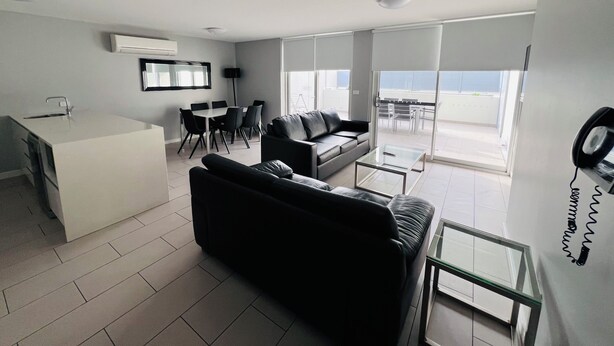 Ein modernes Wohnzimmer mit einer Couch, einem Couchtisch und einem Essbereich mit Stühlen und Tisch. Es gibt einen Balkon mit Blick.