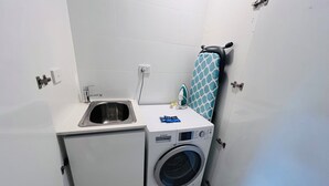 A compact laundry area with a washing machine, a small sink, and a towel rack. - Two Bedroom Apartment (Hamilton)
