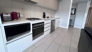 A modern kitchen with white cabinetry, a built-in oven, a dishwasher, and a gas stove. - Two Bedroom Apartment (Hamilton)
