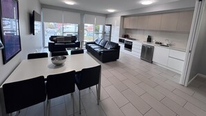 A modern kitchen with white cabinets, a dining area with a white table and black chairs, and a black leather sofa. - Two Bedroom Apartment (Hamilton)