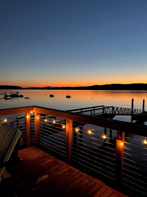 A wooden deck with string lights, overlooking a calm lake at dusk. - Spacious 2 bedroom home with 2 bedroom cabin on the water at Hood Canal. (Belfair)