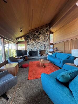 A living room with a stone fireplace, a television, and blue furniture. - Spacious 2 bedroom home with 2 bedroom cabin on the water at Hood Canal. (Belfair)