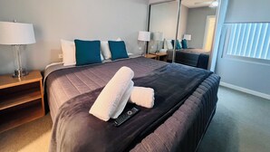A hotel room with a large bed, two bedside tables with lamps, a mirror, and a window with blinds.