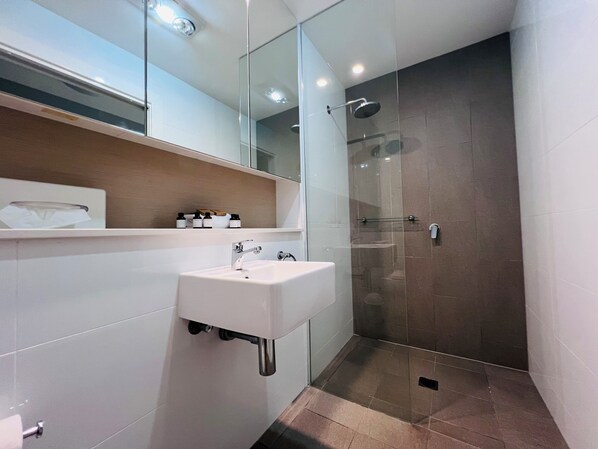 Ein modernes Badezimmer mit einem weißen Waschbecken, einer Duschkabine aus Glas und einem Spiegel über dem Waschbecken.