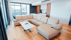 A modern living room with a large L-shaped sectional sofa, a small coffee table, and a view of the city through large windows. - Three Bedroom Cockatoo Lodge (Valentine)