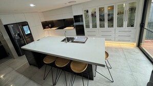 A modern kitchen with a large island, bar stools, and a built-in oven. - Three Bedroom Cockatoo Lodge (Valentine)