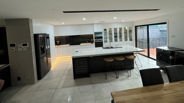 A modern kitchen with white cabinets, a central island with bar stools, and a dining area with a wooden table and chairs. - Three Bedroom Cockatoo Lodge (Valentine)