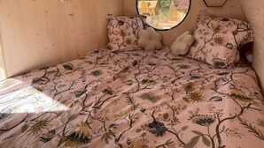 A cozy bedroom with a wooden ceiling, a round window, and a floral bedspread. - Hébergement Insolite Dans L'esprit Tinyhouse: la Tiny Bulle Pour Deux Personnes (Vignot)