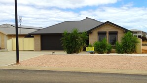 A two-story house with a dark roof and beige walls, a garage, and a driveway. There is a sign for holiday rentals and a small dog in the driveway. - Marina Belle, Wallaroo (Wallaroo)