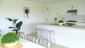 A modern kitchen with white cabinets, a central island with stools, and a potted plant on the table. - Marina Belle, Wallaroo (Wallaroo)