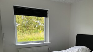 A bedroom with a bed, a window with a view of greenery, and a radiator. - Hytten (Lemvig)
