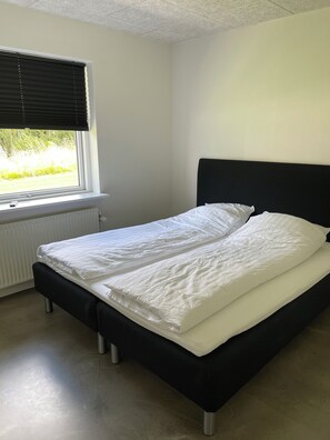 A single bed with a black headboard in a room with a window and radiator. - Hytten (Lemvig)
