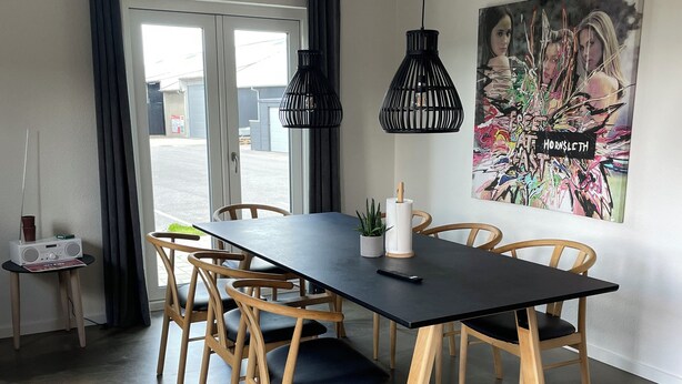 A modern dining area with a black table and wooden chairs, a radio on a side table, and a poster on the wall. - Hytten (Lemvig)