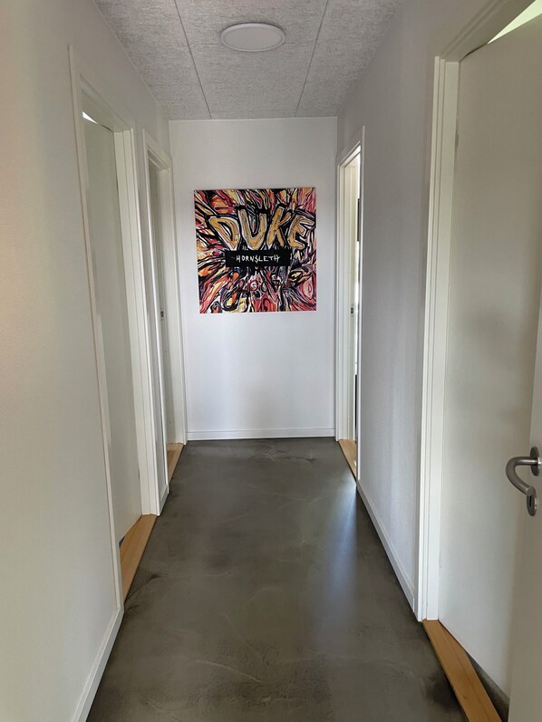 A hallway with a dark floor, white walls, and a door on the right. - Hytten (Lemvig)