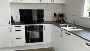 A modern kitchen with white cabinets, a black countertop, a built-in oven, a sink, and a pendant light. - Hytten (Lemvig)
