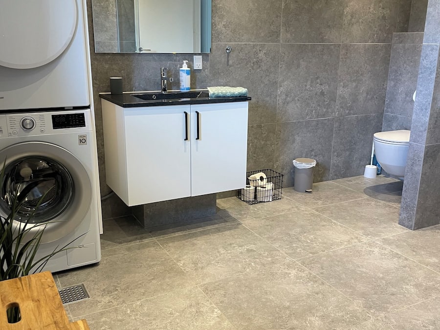 A modern bathroom with a washing machine, a sink with a mirror, and a toilet.
