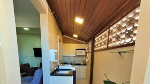 Eine kleine Küche mit Mikrowelle, Spüle und Schränken, die in einen Wohnbereich mit Sofa und Fernseher übergeht.